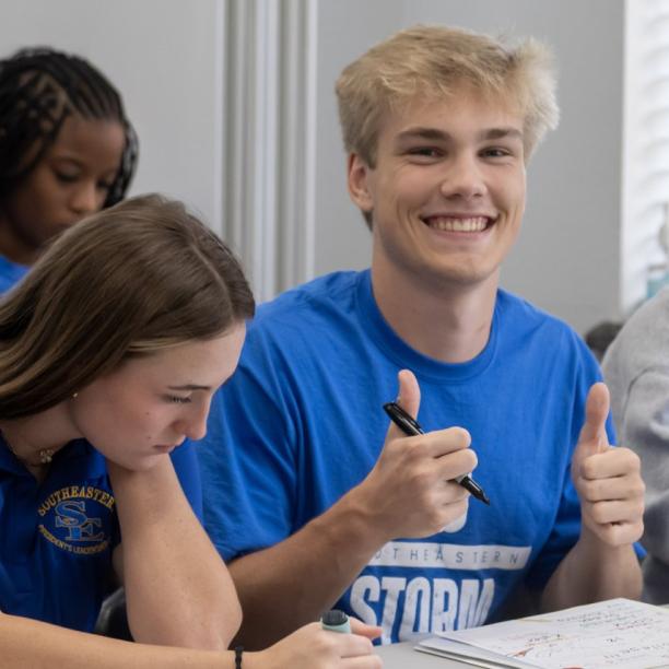 Students smiling one man show their two thumbs