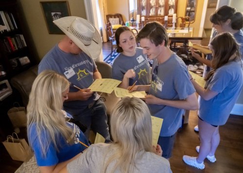 A group of five young adults in casual shirts, engaged in discussion at an outdoor event
