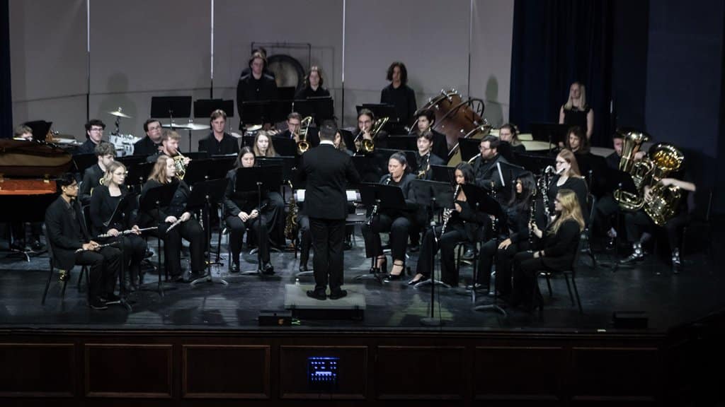 A concert band performing on stage with a conductor leading musicians.