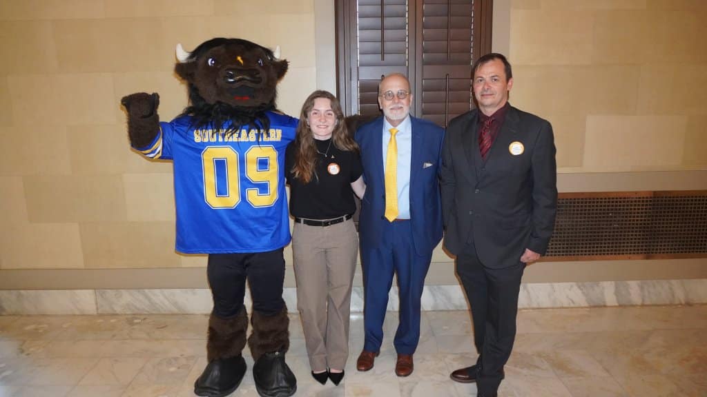 Four people, including a bison mascot, pose for a photo indoors.
