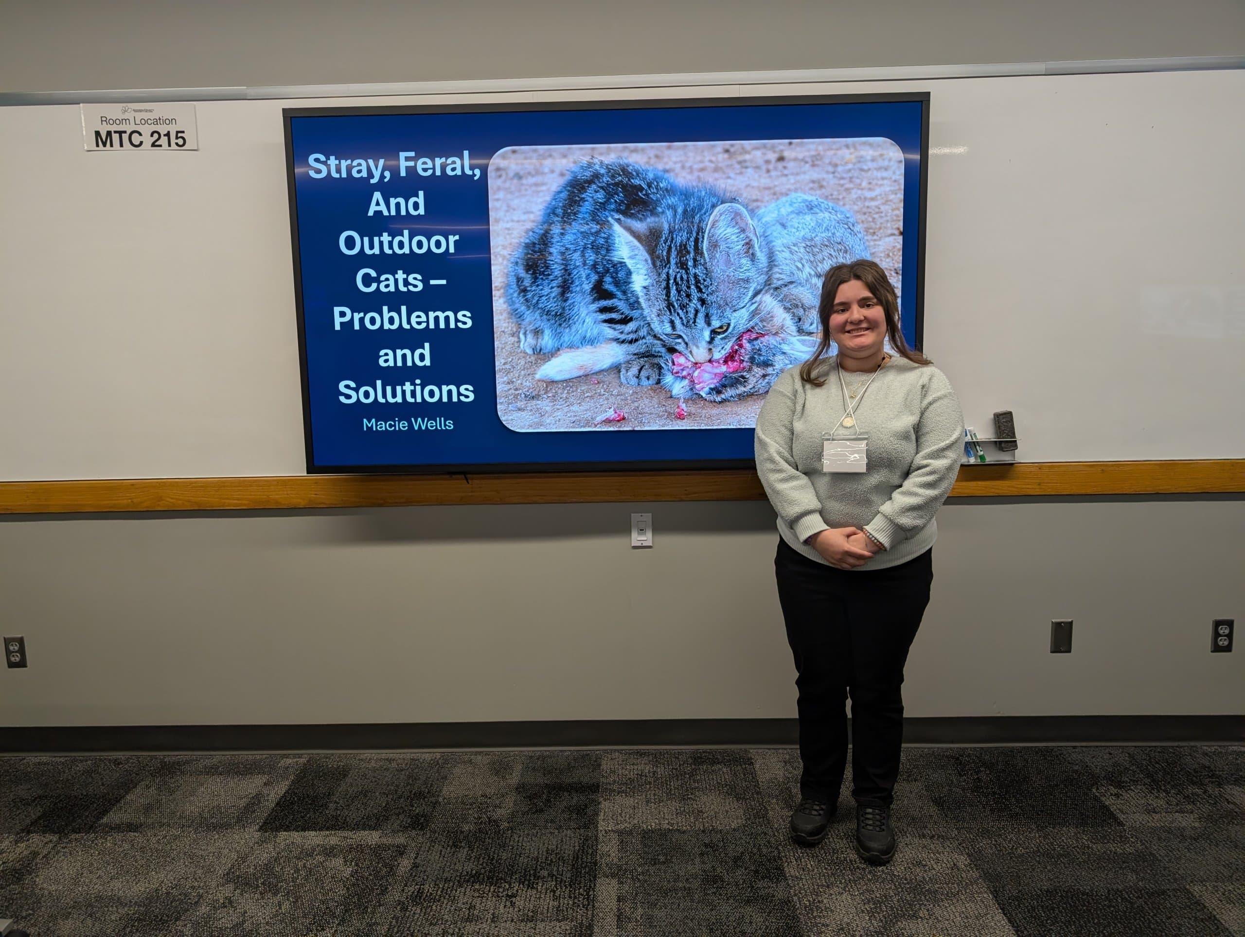 A woman standing in front of a monitor with a cat on it