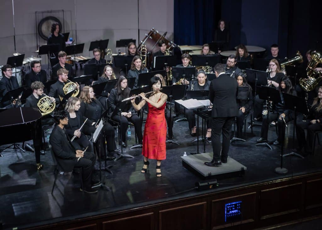 A flutist in a red dress performs with an orchestra and conductor on stage