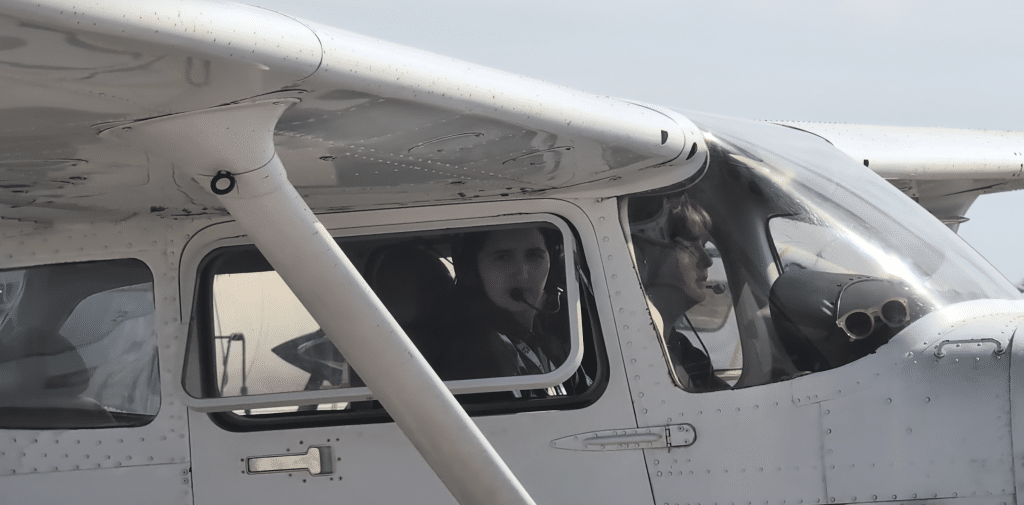 Two people inside a small aircraft cockpit, wearing headsets.
