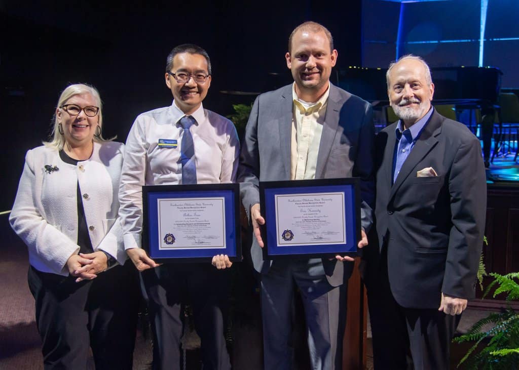 Four people on stage with the middle two holding awards
