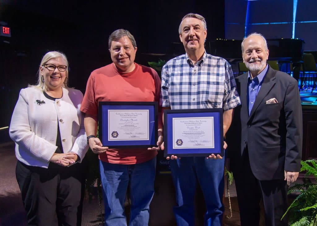 Four people on stage with the middle two holding awards