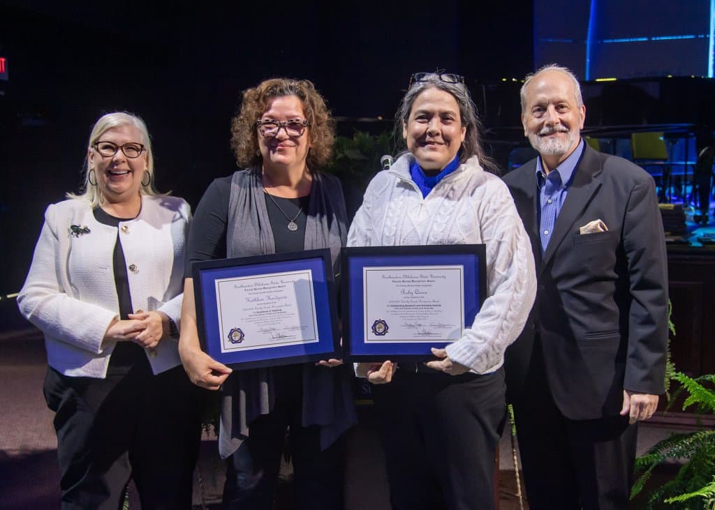 Four people on stage with the middle two holding awards