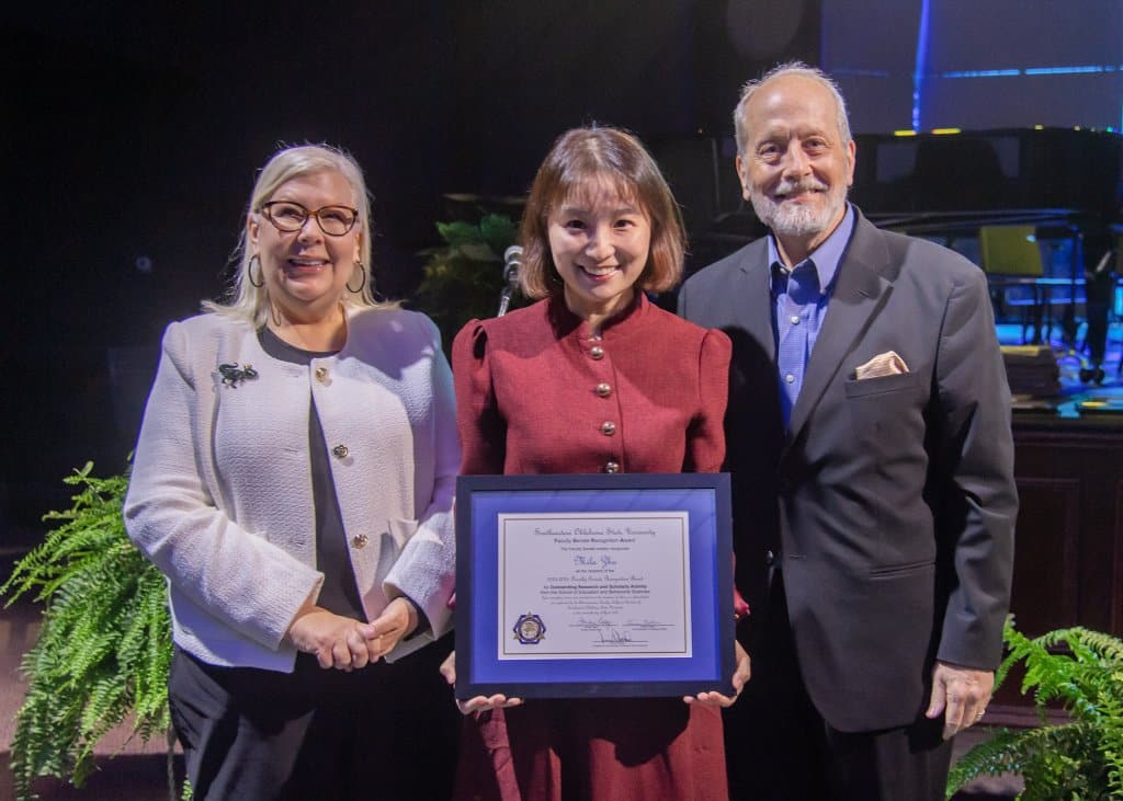 Three people on stage with the middle person holding an award