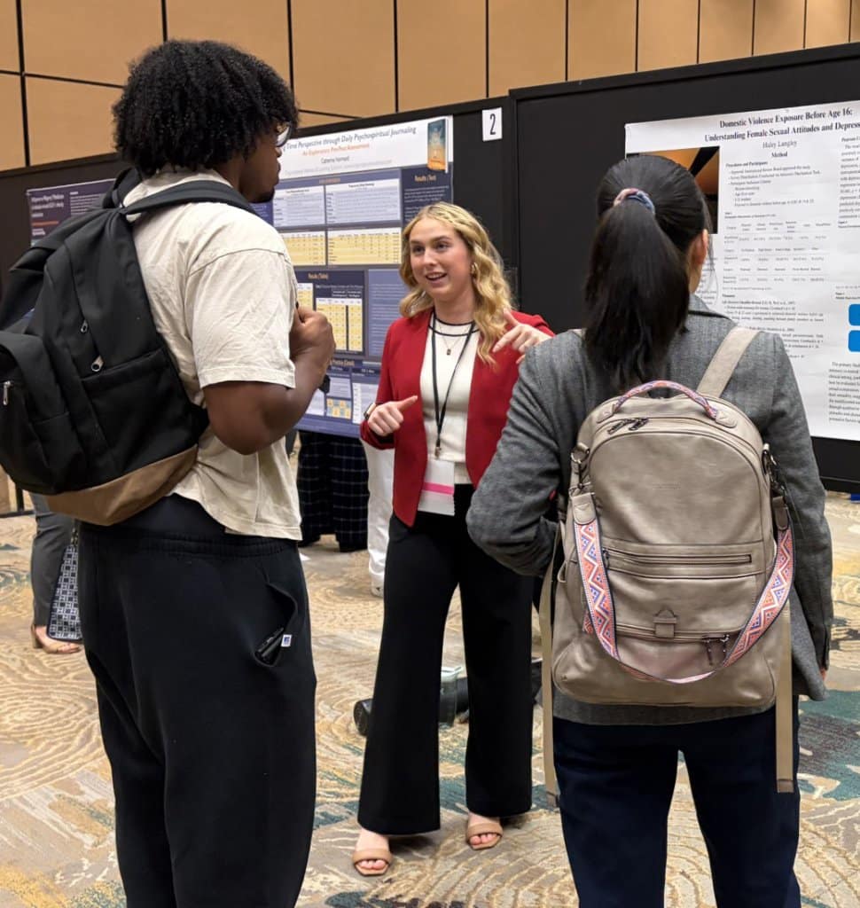 Three people conversing at a conference in front of research posters.