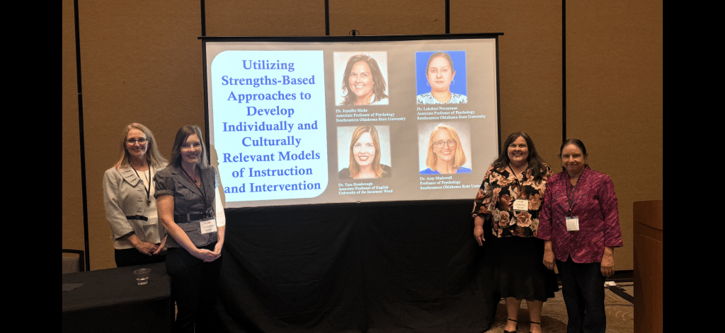 Five women stand beside a projection screen displaying a conference presentation.