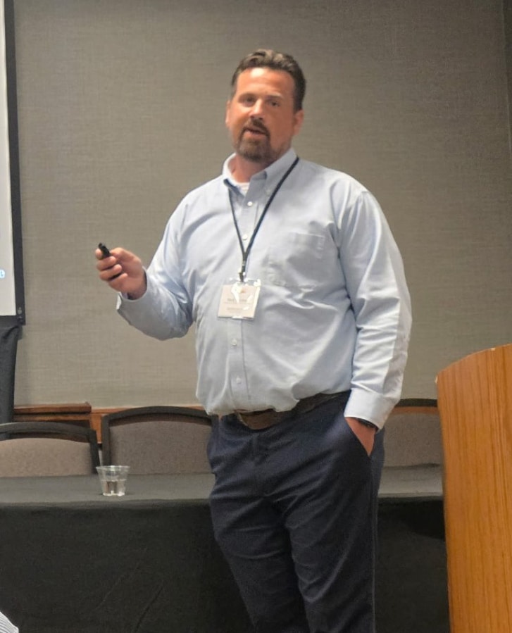 Man giving a presentation in a conference room, holding a remote.