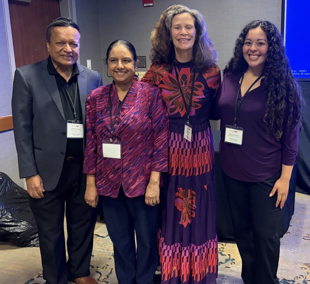 Four people standing together, each wearing name badges, in a conference setting.