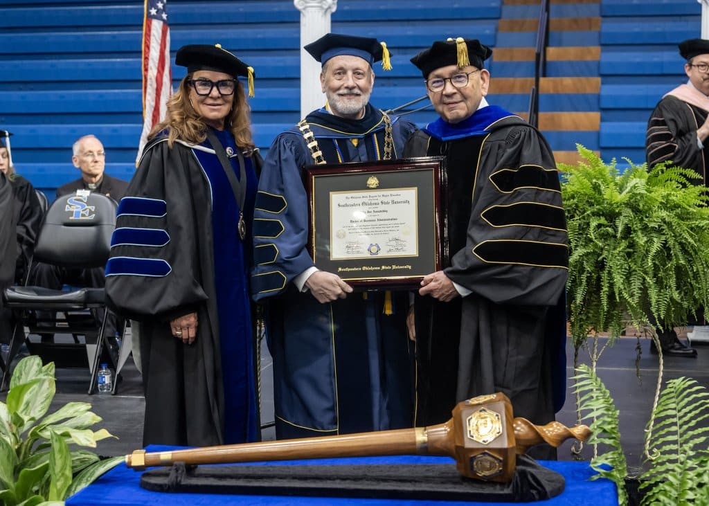 Three people on stage in academic regalia