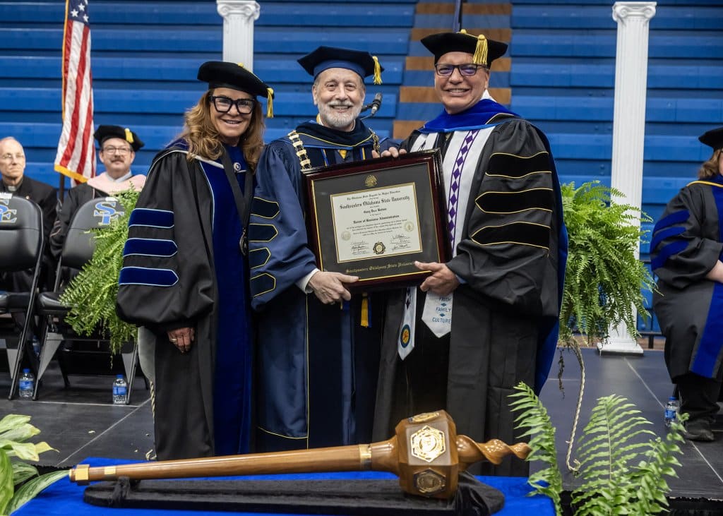 Three people on stage in academic regalia