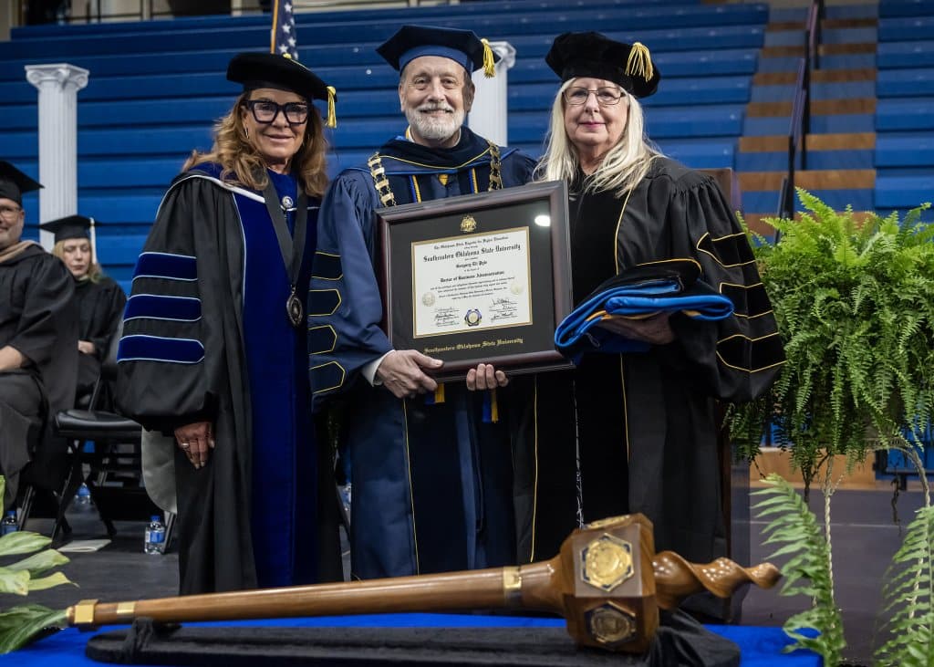 Three people on stage in academic regalia