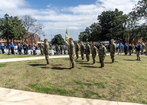 Military personnel in camouflage uniforms with a flag reading GOLD and Oklahoma Army National Guard, Southeastern Oklahoma State University.