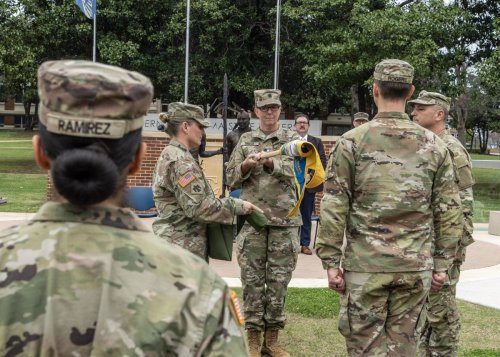 Military personnel in camouflage uniforms with a flag reading GOLD and Oklahoma Army National Guard, Southeastern Oklahoma State University.